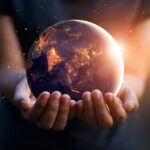 Human hands holding a glowing Earth at night against a dark background, symbolising global impact, trust, and customer testimonials.